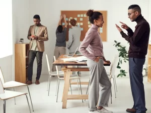 談笑する男女とその後ろでスマホを操作している男性と掲示板の付箋紙を貼ってアイディア出しをしている男性２人の様子