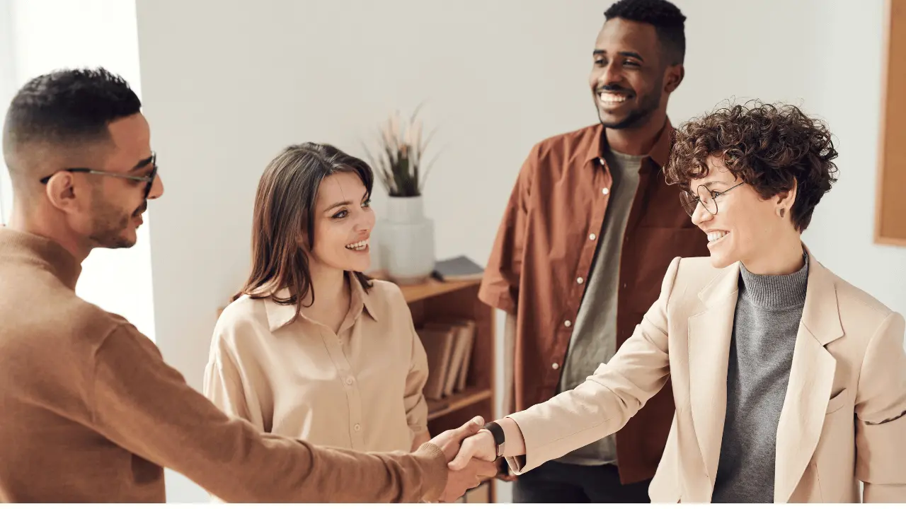 オフィスで、笑顔の男女4人が挨拶を交わし、その内のメガネをけた2人の男女が握手している様子