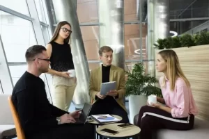 オフィスのラウンジで、丸テープルを囲んで4人の男女が座って打ち合わせをしている様子。