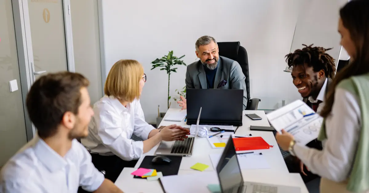 多様なチームが会議室に集まり、笑いも交えながら活発にアイデアを出し合っている。